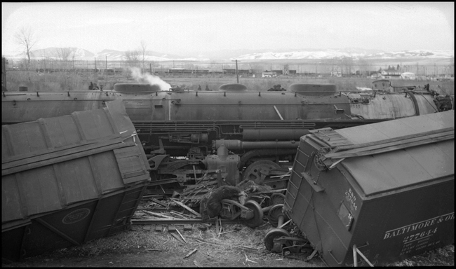 Extra 5121 West rear-ended the main line local, Extra 1816 West, at Drummon, MT. This accident resulted indirectly from the events surrounding the derailment of wrecker 47 east of Missoula (see RVN09581-09595). Missoula engineer Charles F. Reinke and his fireman had been on a layover in Helena when they were called to take Helena wrecker no. 37 to Missoula to help re-rail wrecker 47. In the meantime, officials decided to use a small wrecker from the Missoula car shop to assist wrecker 27 for that job, so Reinke and his fireman were stopped at Garrison and sent back to Helena. Then, after returning to Helena, they were called short of their legal rest period to handle Extra 5121 West. According to railroad officials, as Reinke approached Drummond he and his fireman had probably fallen asleep and missed block signals protecting the rear of Extra 1816 West. Extra 1816 West's conductor looked out the back of his caboose just in time to see the high speed approach of Extra 5121 West, so he ran into the nearby field. His brakemen were already on the ground giving signals for switching moves they were making at Drummond. The big Z-7 4-6-6-4 type locomotive plowed into the local's wooden caboose at high speed. There were only minor injuries to the crews involved. Conductor Emil Berglin was in charge of Extra 5121 West. Engineer Elmer Walkup and Conductor Malcom McCauley were handling the local.