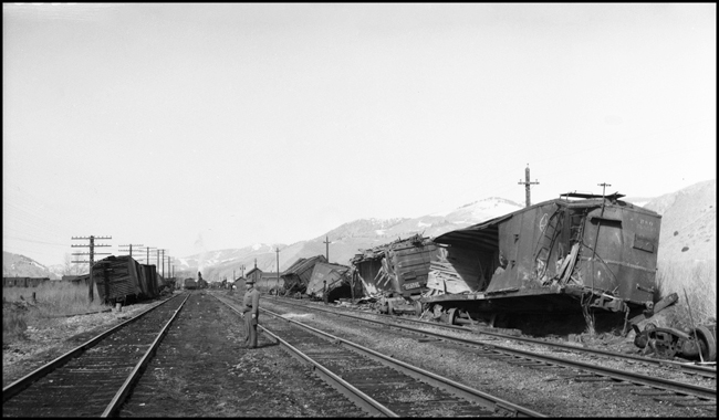 Extra 5121 West rear-ended the main line local, Extra 1816 West, at Drummon, MT. This accident resulted indirectly from the events surrounding the derailment of wrecker 47 east of Missoula (see RVN09581-09595). Missoula engineer Charles F. Reinke and his fireman had been on a layover in Helena when they were called to take Helena wrecker no. 37 to Missoula to help re-rail wrecker 47. In the meantime, officials decided to use a small wrecker from the Missoula car shop to assist wrecker 27 for that job, so Reinke and his fireman were stopped at Garrison and sent back to Helena. Then, after returning to Helena, they were called short of their legal rest period to handle Extra 5121 West. According to railroad officials, as Reinke approached Drummond he and his fireman had probably fallen asleep and missed block signals protecting the rear of Extra 1816 West. Extra 1816 West's conductor looked out the back of his caboose just in time to see the high speed approach of Extra 5121 West, so he ran into the nearby field. His brakemen were already on the ground giving signals for switching moves they were making at Drummond. The big Z-7 4-6-6-4 type locomotive plowed into the local's wooden caboose at high speed. There were only minor injuries to the crews involved. Conductor Emil Berglin was in charge of Extra 5121 West. Engineer Elmer Walkup and Conductor Malcom McCauley were handling the local. This view, looking west and taken a few days after the accident, shows at least one main track restored to service as cleanup continues. The cars in the foreground are from the Extra 5121 West. Locomotive no. 5121 is being re-railed by the wrecker in the distance.
