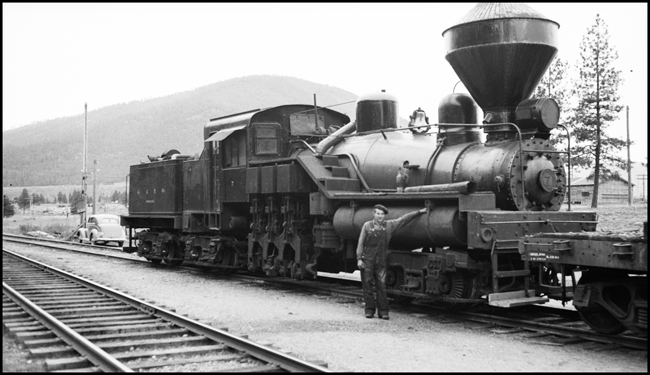 ACM 7, shay locomotive with Mr. Elwood Bogard standing by locomotive.  Cyclone style spark arrester stack on locomotive.  Right side view.