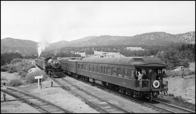 Some passengers, possible company officials are riding the back platform of the North Coast Limited.  One is concentrating on the camera.  Another is ready to give the local in the siding a quick once over.