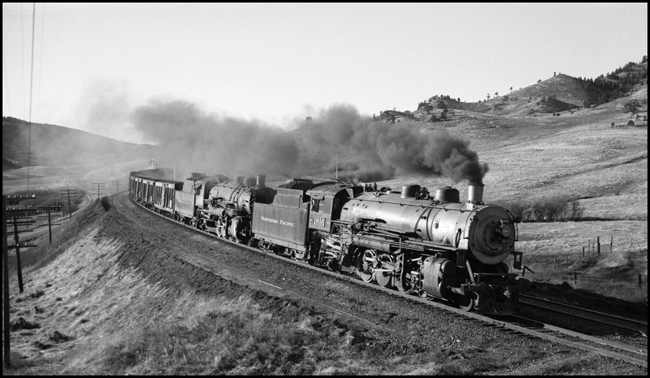 A W-3 and a W-5, NP's best Mikados, with a little help froma pusher at the end of the train, get a move on some fairly hot freight.  Stockcars are in the standard position, right behind the engines.