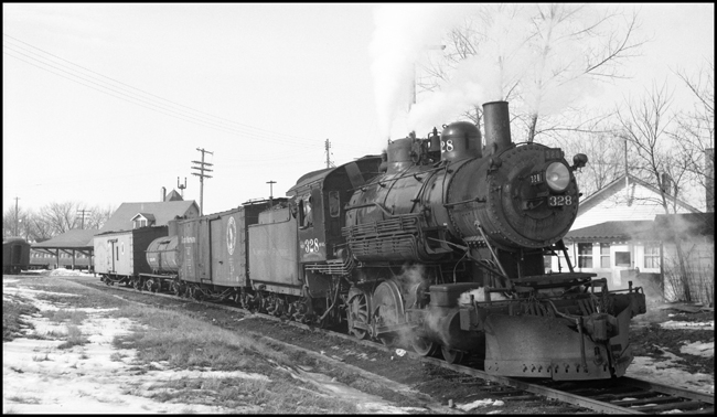This is a mixed train on the Taylors Falls branch line.  The combination baggage/passenger/mail car has been cut off the train in order to switch one or more of the freight cars.  The class S-10 328 was part of a group of locomotives built for another railroad, and purchased by NP when that railroad defaulted on the order.  The 328 was saved after dieselization, and for many years pulled excursion trains in northern Minnesota.  In 2006 it may be found in the Jackson Street Roundhouse in Minneapolis awaiting rebuilding.