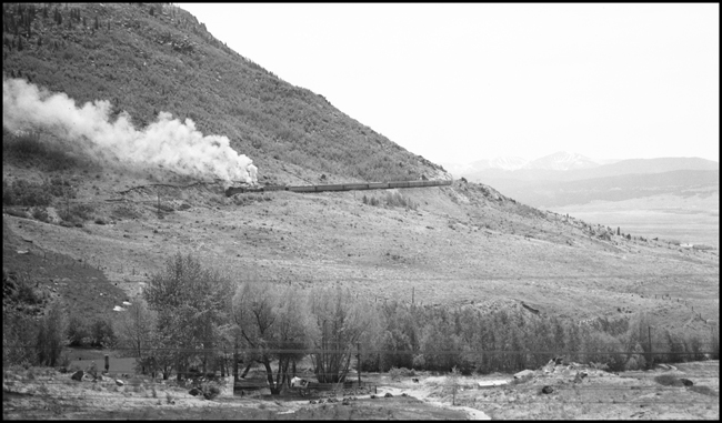 Looking from vestibule of NP No. 1 across valley to track climbing Butte Mtn, with eastbound No. 4, steam helper pushing, in distance.