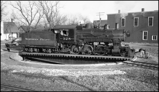 NP 328, Class S-10, on Strong arm turntable at Grantsburg, WI, while 3 men labor to turn locomotive by pushing on turntable arms.
