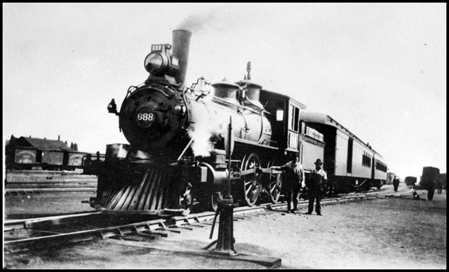 NP 688, a 4-4-0 American Std Class and former NP 346 with a passenger train at Helena.  Engineer Jack Furlong and Baggage-man B. P. Townsend are in the foreground and Conductor J. V. Logan is in the background.