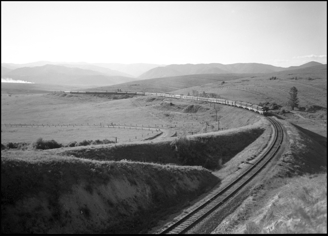 A big train under a big sky.  The Mainstreeter heads west with five diesel units and a long string of head end cars, normal, up front, and a long string of heavyweight foreign cars to the rear