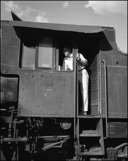 Not correctlyly dressed for the working environment, but making the best of it, a man shopping for a steam locomotive explores the cab of a logging railroad Shay