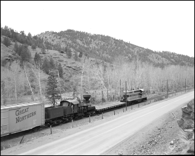 The steam engine in tow has a rider, standing in the gangway as it is hauled north.  Many large or valuable or unusual shipment have human escorts, usually called expediters, working to see that all stays well en route.