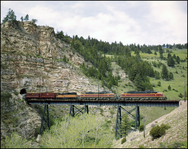 An eastbound freight extra, powered by two streamlined Little Joe electric locomotives and a GP9, has emerged from the east portal of Eagle Nest Tunnel.  The lead unit is one of the two Little Joes that was fitted for passenger service, a purpose gone now that the Olympian had been discontinued for a year
