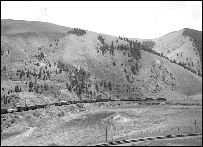 With the parallel Northern Pacific mainline in the foreground, a Milwaukee road fast freight west has plenty of power for its mixed consist.  Two GE built streamlined electrics lead three 1750 horsepower general purpose diesels