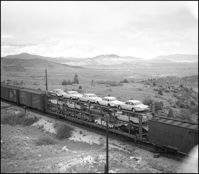 14 Chrysler products, model year 1962, are riding west on a tri level auto rack on Milwaukee Road train 263, somewhere in Montana.
