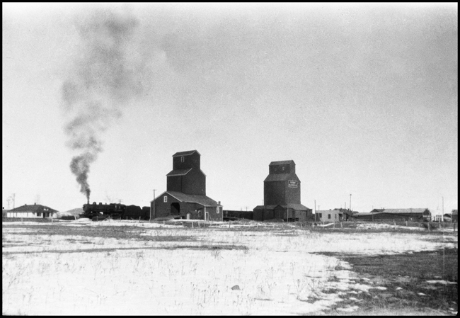 An extra west bound freight passing grain elevators at Roberts, MT about 1926.