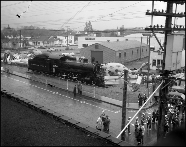 Rubber animals on display in front of Missoula NP depot, with photo taken from the telegraph office window.  Marching band also in picture.