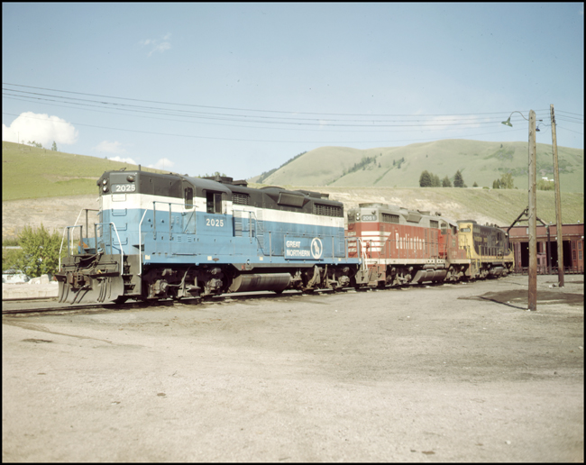Color photo of GN 2025, BN 2061 CBQ red paint, and NP 333 coupled BN engine faciltiy Missoula, MT note snow plow on GN 2025.