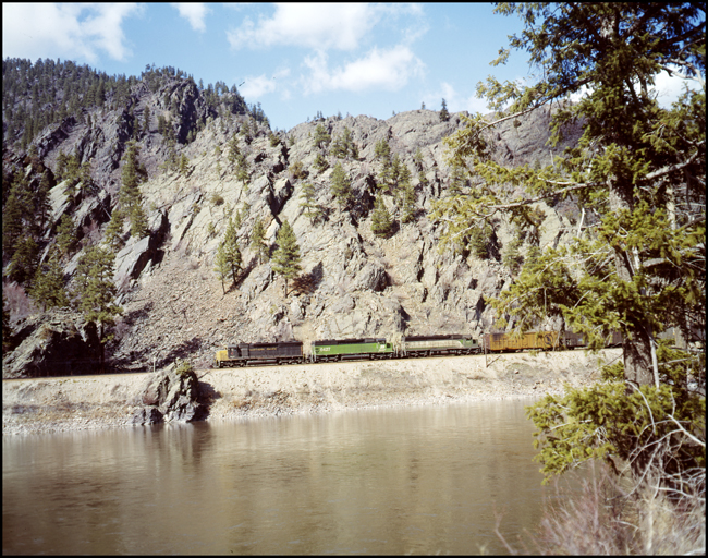Color photograph of BN extra 6415E with 6415 in NP paint near Weeksville, MT. with Clark Fork river in foreground.  All units in consist are SD45s with third unit in the CBQ green with white paint scheme.
