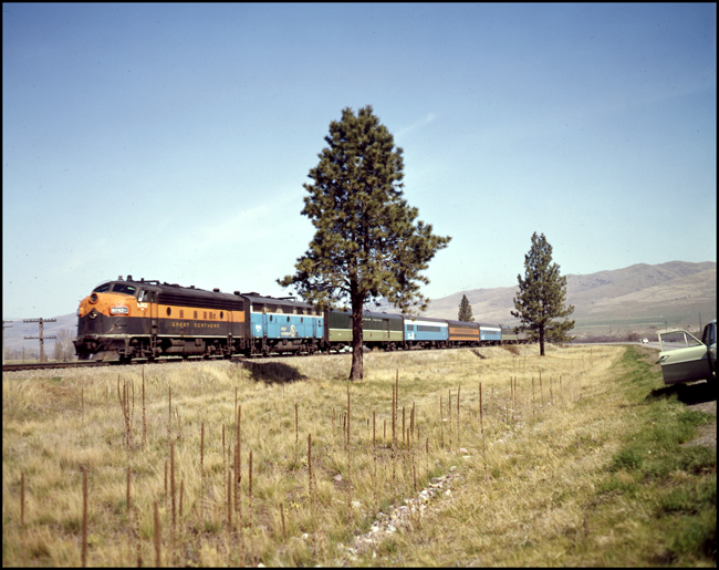 Color photograph of BN passenger train #30, BN 9742, in GN modern orange and green paint near Ravalli, MT.  This is the last run of this train. There are six cars in train.  Bn crew is Young and Schultz.