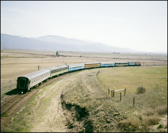 Color photograph going away of BN passenger train #30, BN 9742, in GN modern orange and green paint west of DeSmet, MT.  This is the last run of this train. There are six cars in train.