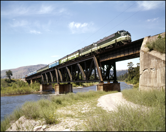 Color picture of Amtrak passenger train east bound with BN 9802 on point in NP paint on bridge near Bonner, MT.  Second F unit in consist is an A unit in NP paint and third and fourth units are BN Funits in the BN passenger paint scheme..