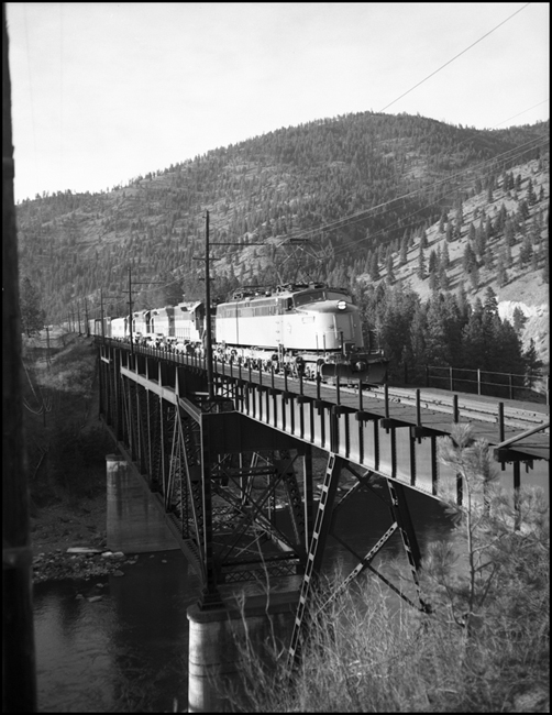 MILW No. 262 with electric lead locomotive and diesels following in consist, crossing bridge near Cyr. 