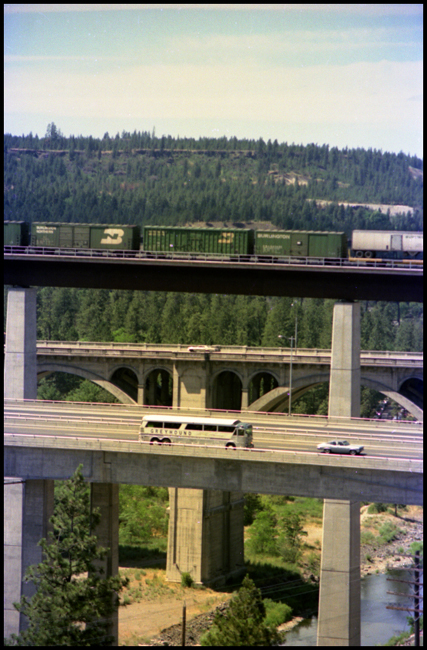 BN Extra freight on Bridge at Spokane, WA. Greyhound bus crossing on highway bridge.