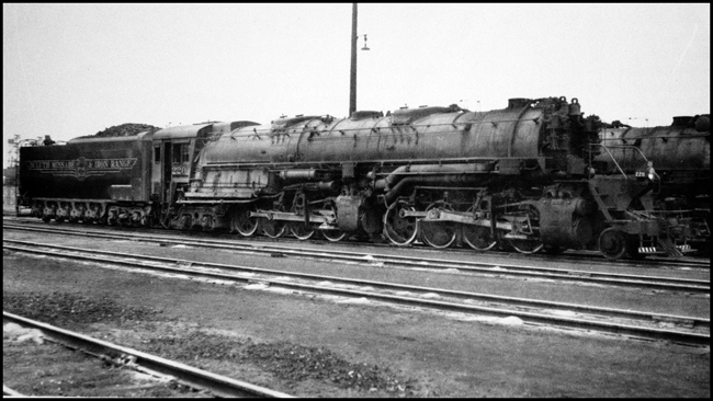 Dirty after a hard run from the iron mines to the north, a Baldwin Yellowstone rests at an engine terminal above thwe Lake Superior shore.  This engine would be one of the last large steam freight engines in regular service in the US, running until the summer of 1960.
