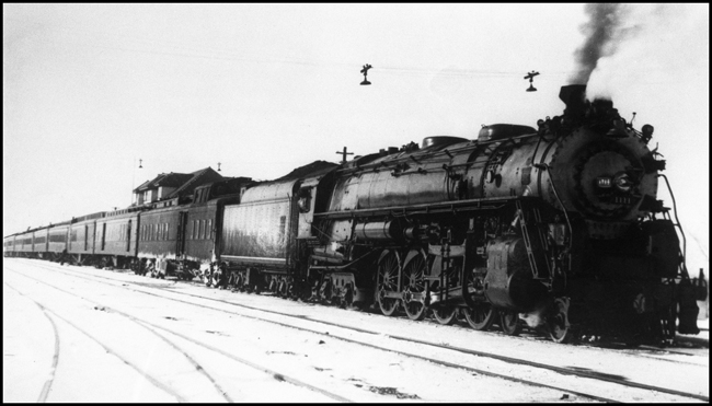 The famous 2626, when it was still demonstrating as Timkin Roller Bearings traveling salesman, the Four Aces, pauses with dynamometer car and westbound North Coast Limited at Jamestown during Christmas rush season.  Note the two Railway Post Office cars.