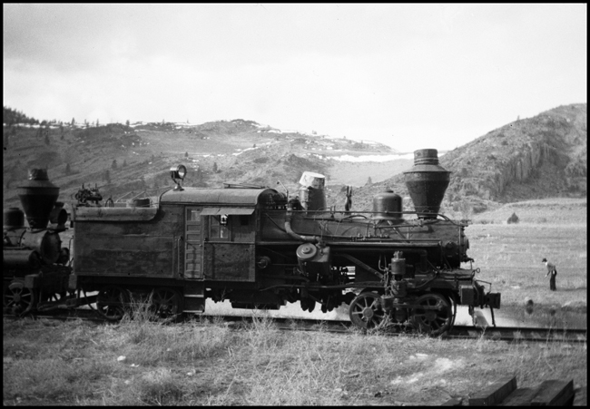 A western Montana golfer shows no interest in a pair of retired logging locomotives stored on a lightly built track.  The lead engine is a Heisler, a product of the Stearns Manufactruring Company of Pennsylvania, builder of about 600 specialized locomotives.
