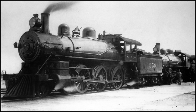 NP 258, Class P locomotive coupled onto the head end of another steam locomotive, with several workman along side locomotives.