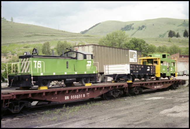 Parade toys including switcher, gondola and caboose in BN colors loaded on two flat cars at Missoula