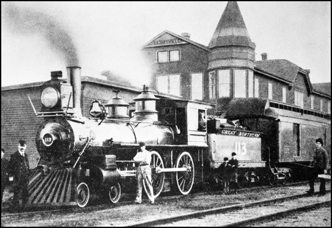 GN 113 on passenger train arriving into Barnesville, MN with crew and on-lookers posing for photo.