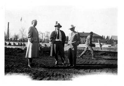 Three people stand where the new library is being constructed, 1948