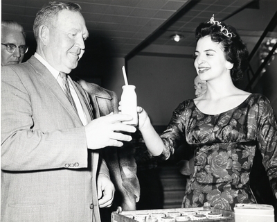 A woman passes a glass of milk to a man during the D.M. Short Course, 1958/1959