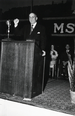 A speaker, with his hand raised, at Montana State College