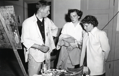 An artists shows two students his paints and painting.
