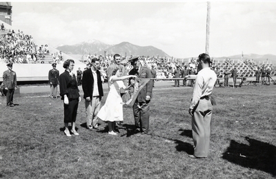 A woman attaching something to the top of a Bobcat flag.