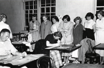 A group of women observe a group of drafting students.