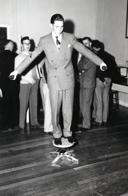 Montana State student balancing on a stool, holding weights in his hands.