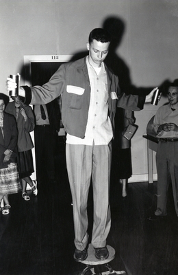 Student balancing on a stool, while holding something in his hands.