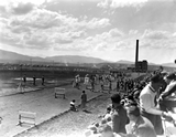 Students sitting in bleachers watching a procession of athletes with heating plant in background