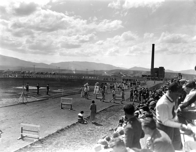 Students sitting in bleachers watching a procession of athletes with heating plant in background