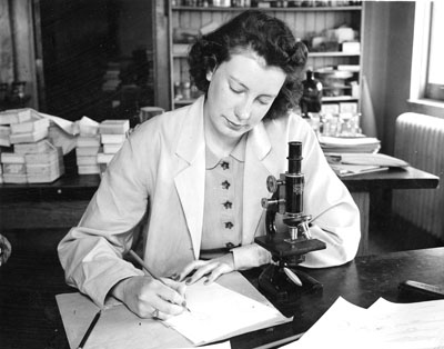 Student sitting at desk writing on a tablet with microscope near