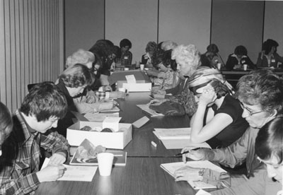 Women sitting at long tables, filling out paperwork at the Women Aware Conference
