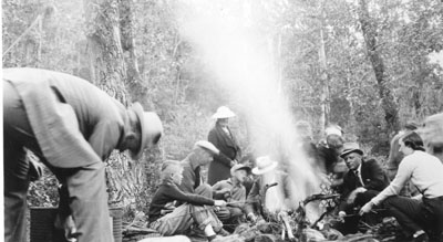 People surrounding a campfire, making food