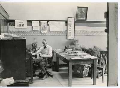Extension agent sitting at desk, 1921