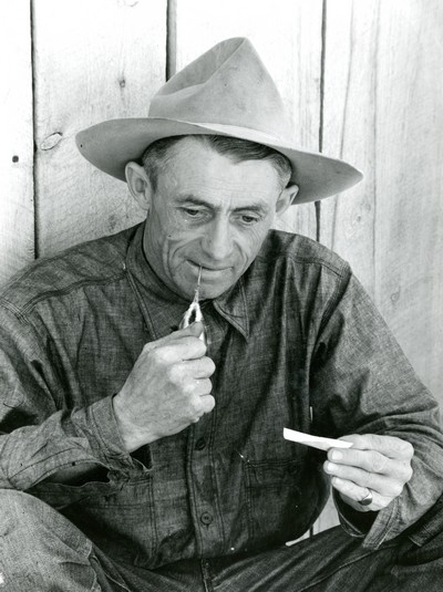 Portrait of Jack Arnold, Part owner of the Montana Quarter Circle U Ranch Hand rolling a Cigarette.