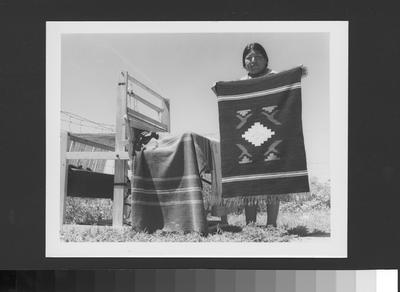 Arapaho Weaver Standing by Loom With Finished Woven Blankets