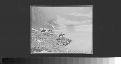 Photo of people on horseback on the edge of a lake in Glacier National Park