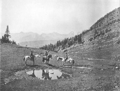 Photo of three people on horseback watering their horses at a small pond in Glacier National Park