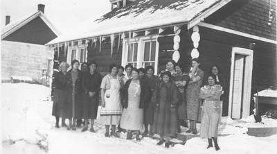 Photo of 17 women standing in front of a log structure in the winter, Browning, Montana.