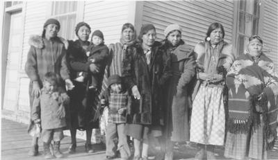 Black and white photo of a large group of Blackfeet women and children waiting outside the train depot.